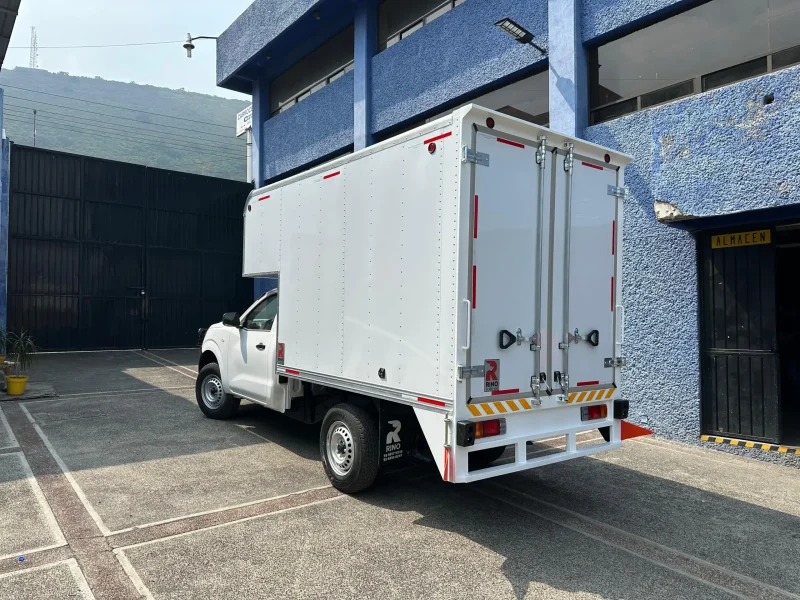 Camión de carga con caja seca y copete estacionado en patio con flota al fondo